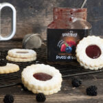 biscotti disposti sul piano da lavoro e vasetto di confettura frutti di bosco aperto